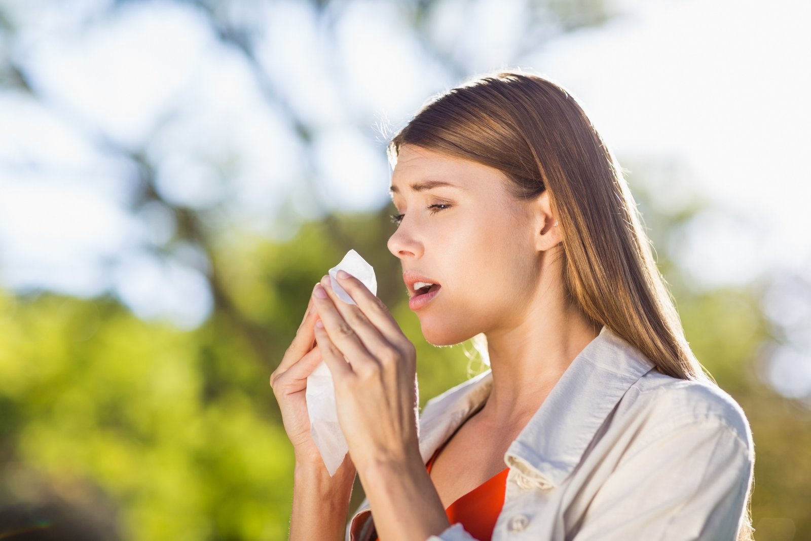 Beautiful woman using tissue while sneezing in park